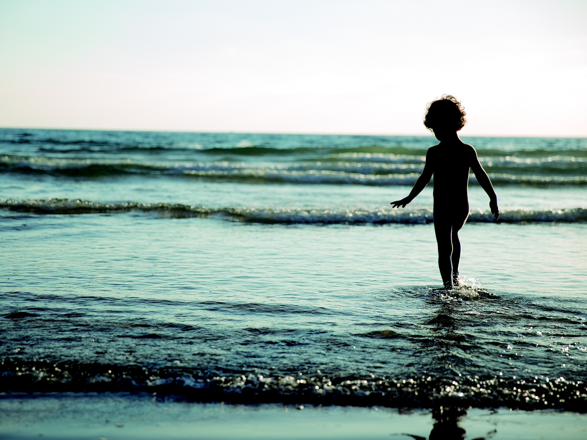 Niño en la playa entrando en el agua al atardecer